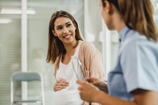 Attractive pregnant woman talking to nurse while waits for gynecologist check up.