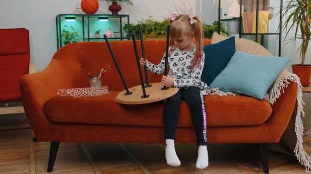 Portrait of Caucasian little children girl collects new modern wooden furniture desk table. Small cute school toddler child kid busy in assembling at home alone. Interior items store ad, hobby concept