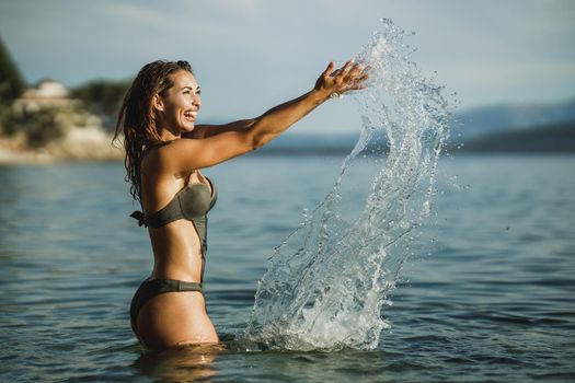 An attractive young woman having fun and splashing in the sea water. She enjoying at vacation.