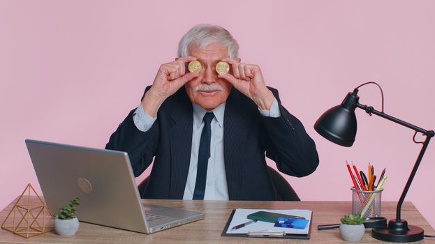 Elderly businessman showing golden bitcoins. Achievement career wealth, cryptocurrency investment mining money income future technology. Senior man freelancer fooling, making faces at office
