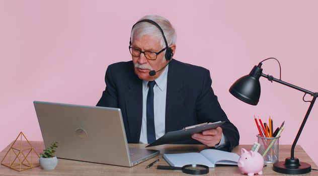 Senior businessman wear wireless headset making conference video call on laptop. Male elderly professional call center agent, operator having distance webcam chat job interview on computer in office