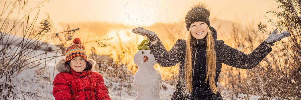 Happy family in warm clothing. Smiling mother and son making a snowman outdoor. The concept of winter activities. BANNER, LONG FORMAT