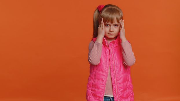 Toddler young children girl kid rubbing temples to cure headache problem, suffering from tension and migaine, stress, grimacing in pain, high blood pressure isolated alone on orange wall background