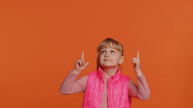 Toddler children girl showing thumbs up, pointing up empty place, advertising area for commercial text, copy space for goods promotion. Young one little child kid isolated on orange studio background