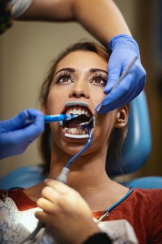 The beautiful young woman is at the dentist. She sits in the dentist's chair and the dentist sets braces on her teeth putting aesthetic self-aligning lingual locks.