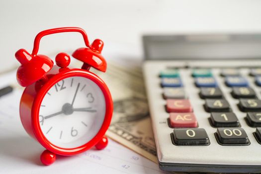 Alarm clock with coins on US dollar banknotes, finance installment loan time.
