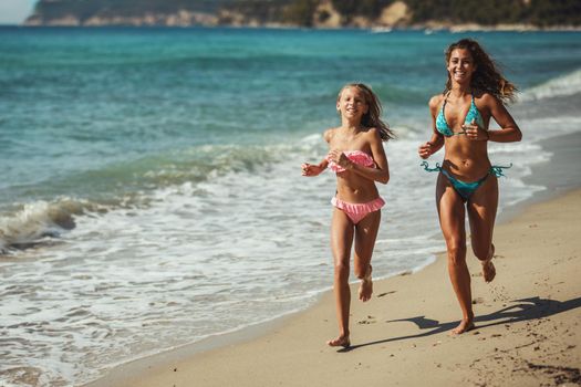 Beautiful teenage girl is enjoying with her mother on the beach. They are running on the seashore and having fun. 