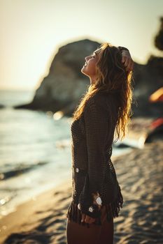 A beautiful young woman is having fun and relaxing on the beach at the sunset. 