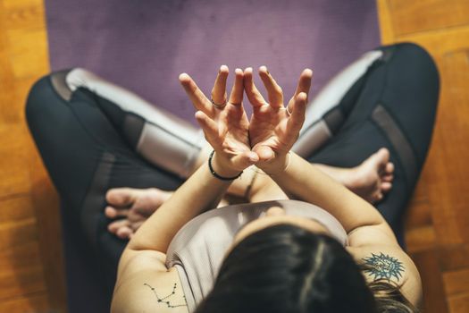 Top view of a young woman is doing yoga Lotus mudra - symbol of purity, this mudra opens the heart. She is meditating on floor mat in morning sunshine at home.