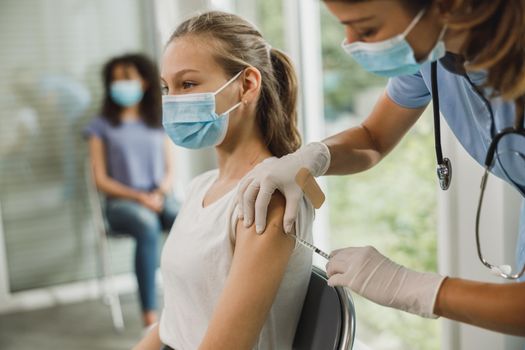 Nurse giving the Covid-19 vaccine to a cute teenager girl due to pandemic.