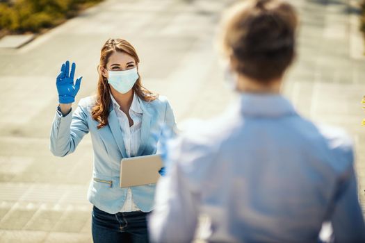 Young business woman with protective mask on her face is going to work at they say hello to her friend during covid19 pandemic.