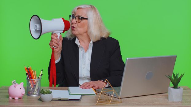 Cheerful senior business woman manager screaming in loudspeaker megaphone horn, discounts news and sales, Hurry up, announcement, advertising. Freelancer sitting at laptop in green chroma key office