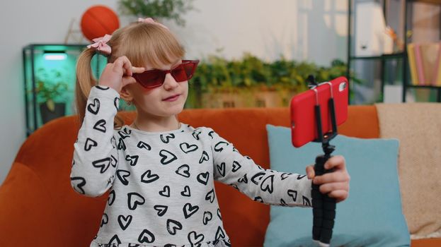 Portrait of Caucasian little happy child girl enjoying conversation on mobile phone with friend relaxing sitting on couch in living room. School toddler kid at home alone. Communication teens concept