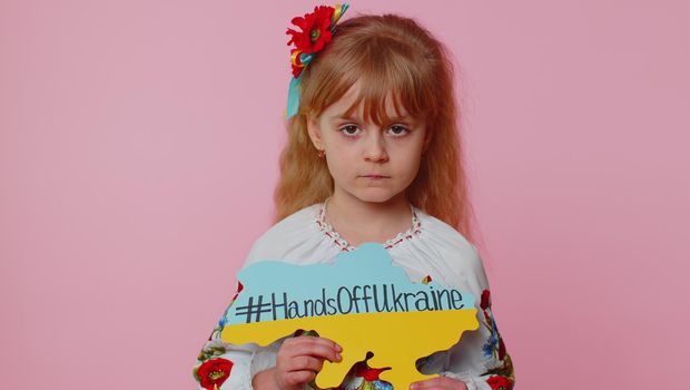 Portrait of Ukrainian girl child in embroidery dress showing banner with massage inscription text on map Hands Off Ukraine. Asking for help. Crisis, war, no peace, stop aggression from Russia country