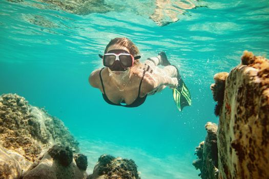 A beautiful young woman is having fun at summer vacation exploring seafloor during scuba diving in sea.