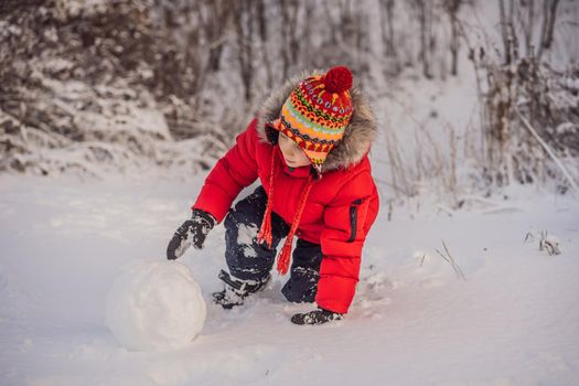 Cute boy in red winter clothes builds a snowman. Winter Fun Outdoor Concept.