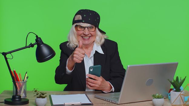 Happy excited funny stylish senior businesswoman use smartphone typing browsing say wow yes, great big win good news shocked by sudden victory at office. Elderly woman on chroma key studio background