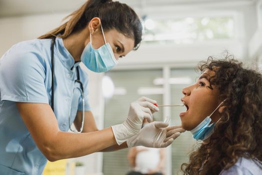 An African American teenager girl having swab medical test from throat during coronavirus pandemic.