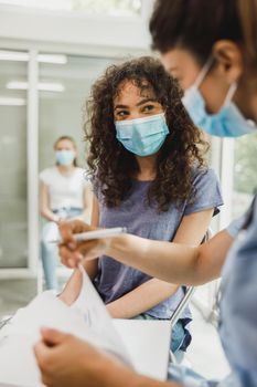 A nurse's writing African American teenager girl patient's data in medical record at waiting room of a clinic.