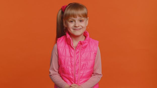 Cheerful happy toddler little girl wearing blouse, vest looking smiling at camera. Young fashion model child kid with brown eyes indoor studio shot isolated on orange background. Female nature beauty