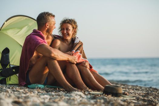 An affectionate young couple spending day at the beach and enjoying sunset wrapped in a blanket.