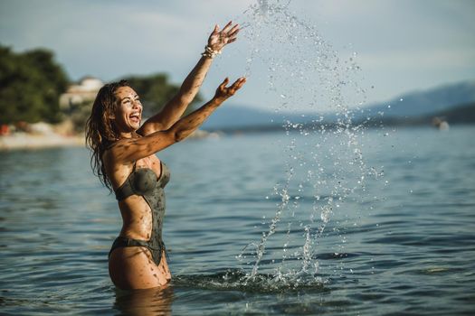 Cheerful young woman having fun on the beach. She is splashing in the sea water and enjoys on vacation.