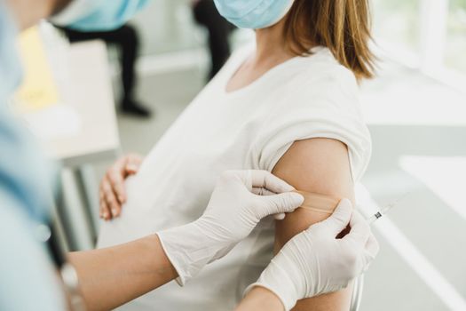 Close-up of a nurse applying a band aid to a young pregnant woman after receiving a vaccine due to coronavirus epidemic.