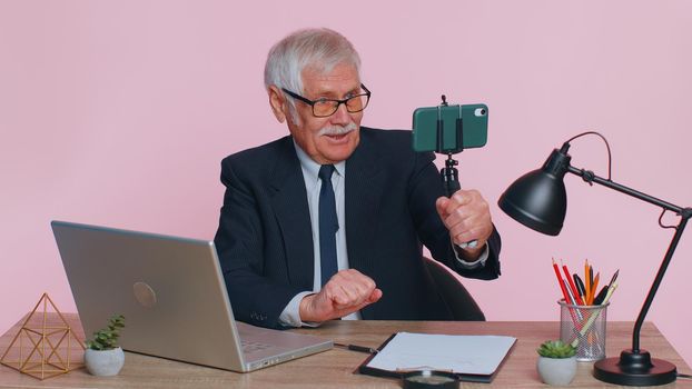 Senior businessman blogger making mobile phone conference video call vlog. Mature professional call center agent, operator having distance smartphone webcam chat job interview on computer in office
