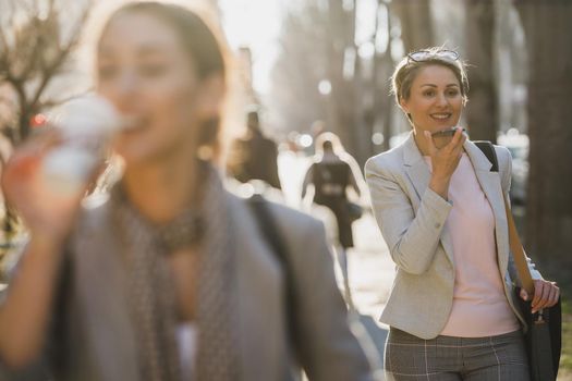 A smiling mature business woman talking voice message on a smart phone while going to work through the city.