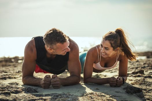 A beautiful couple is doing push-up exercises at the sea beach in summer sunny day.