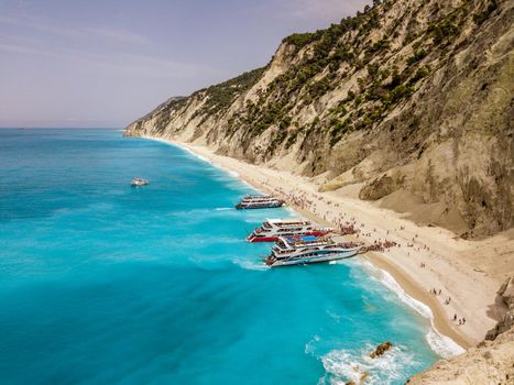Aerial view from drone of amazing azure beach with rocky mountains and clear turquoise water of Mediterranean sea at sunny day. Tourist boats anchoring on the Egremni beach on Greek island Lefkada.