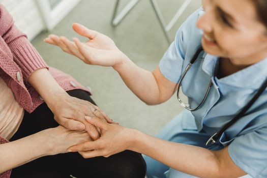 Close-up of caring doctor comforting senior female patient and holding her's hands in waiting room at the hospital.