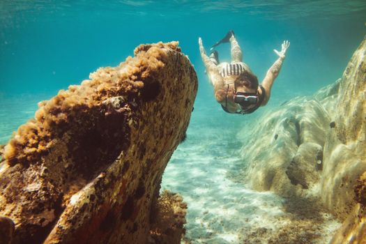 A beautiful young woman is having fun at summer vacation exploring seafloor during scuba diving in sea.