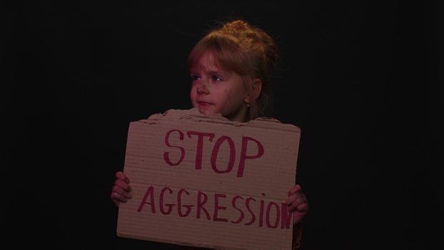 Upset afraid poor toddler child girl kid homeless with dirty face protesting war raises banner with inscription massage text Stop Aggression on black background. Crisis, peace, no war. Family conflict