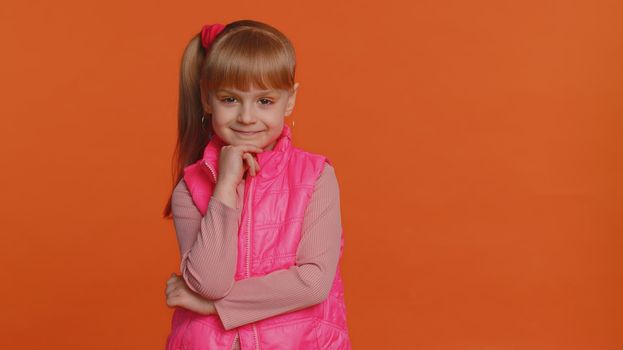 Cheerful lovely toddler little girl wearing blouse, vest looking smiling at camera. Young fashion model child kid with brown eyes indoor studio shot isolated on orange background. Female nature beauty