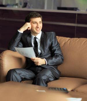 Relaxed businessman sitting at Desk in front of the Windows of the office holding .