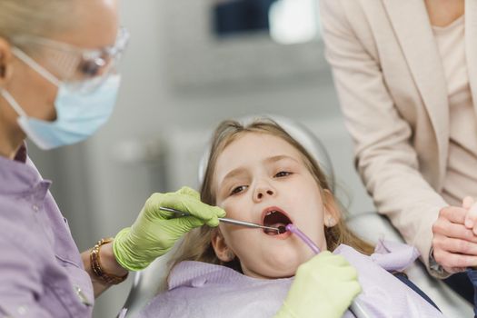 A female dentist examining cute little girl's teeth during dental procedure at dentist's office.