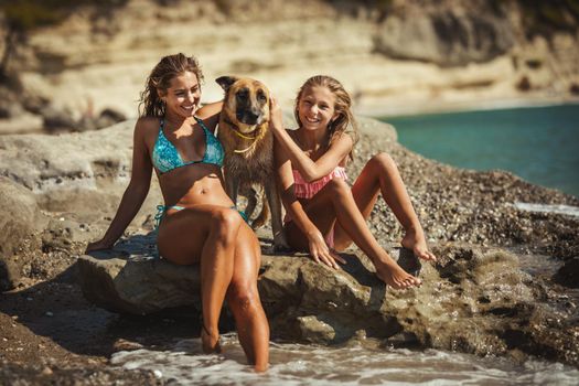 Beautiful teenage girl is enjoying with her mother on the beach. They are sunbathing on the seashore and having fun with their pet dog.