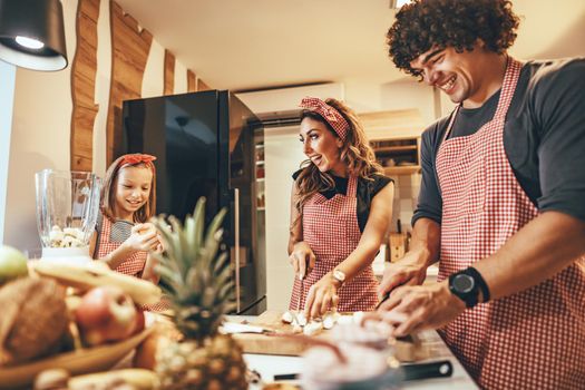 Happy parents and their daughter cooking together in the kitchen while little girl helping them.