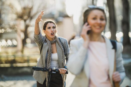 Shot of a furious young business woman riding an electric scooter during morning traffic jams.