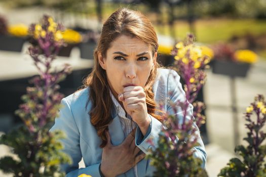 Young businesswoman on break outside coughing due to allergies or colds.