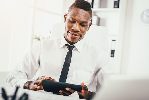 Satisfied African businessman working on digital tablet in modern office.