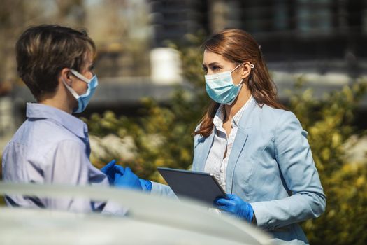 Young business colleagues with protecting masks on their faces are analyzing project outdoors and talking about it while using digital tablet.