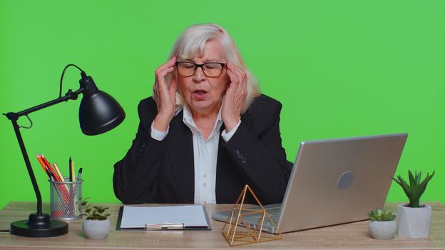 Displeased senior businesswoman rubbing temples to cure headache problem, suffering from tension and migraine, stress, grimacing in pain high blood pressure at office. Elderly woman green chroma key
