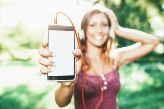 Young woman with headphones is  listening her favorite song and showing display of mobile phone.