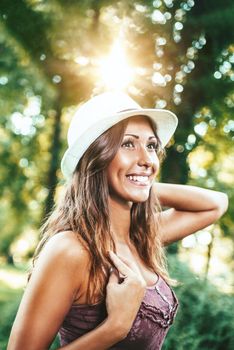 Attractive young woman with summer hat is enjoying her time outside in park with sunset in background.