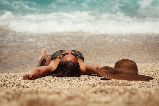 Happy woman is holding straw hat and enjoying sunbathing at beach by the ocean.