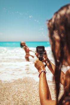 Woman with waterproof action camera takes a photo of her loving daughter in sea waves on the tropical beach. Selective focus. 