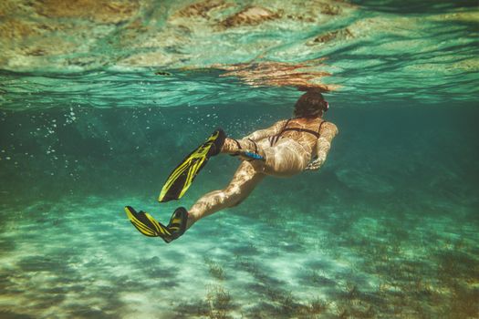 A beautiful young woman is having fun at summer vacation exploring seafloor during scuba diving in sea.