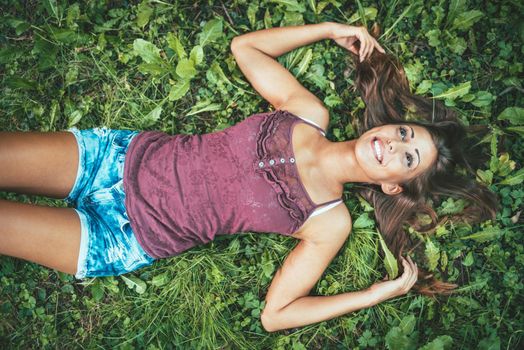 Top view of a happy beautiful young woman  who is lying down on the meadow in summer and looking away.